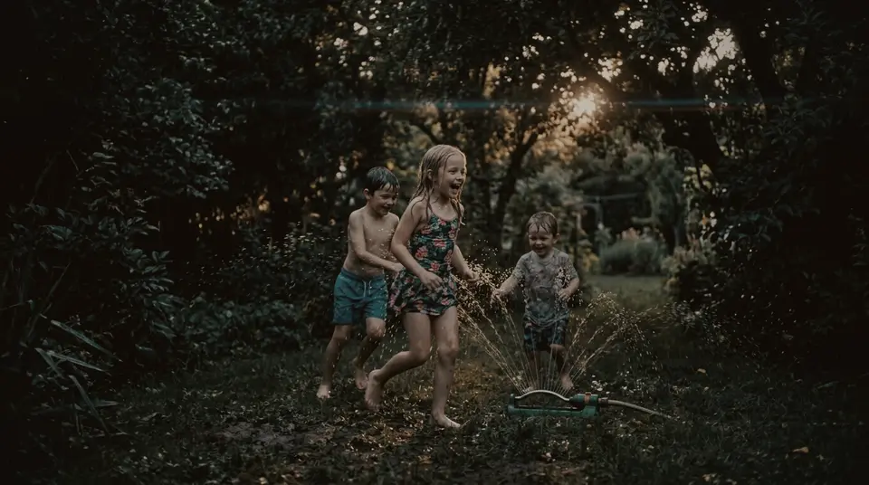 Kinder spielen am Sommerabend im Rasensprenger im gepflegten Garten